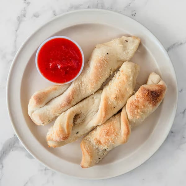 Four twisted breadsticks with parmesan cheese and herbs, served with a side of marinara sauce.