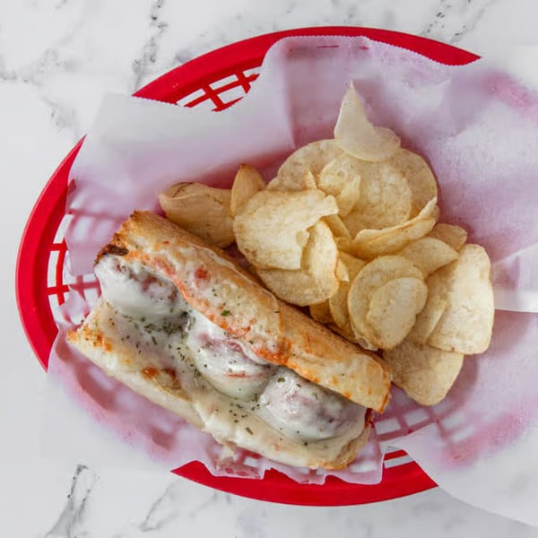 Meatball sub sandwich with melted cheese and potato chips in a red basket.