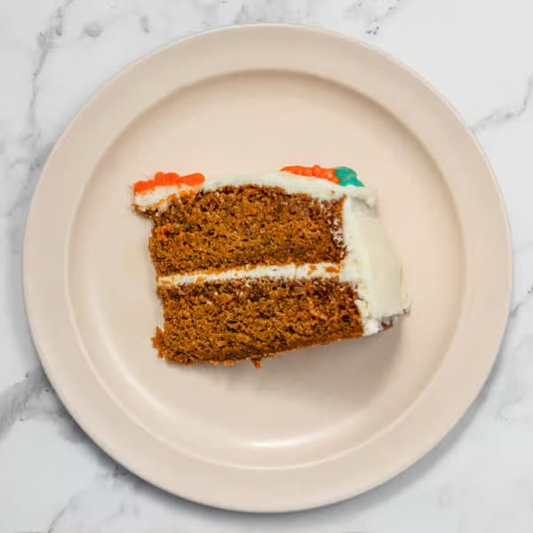 A slice of carrot cake with white frosting and orange and green carrot decorations on a plate.