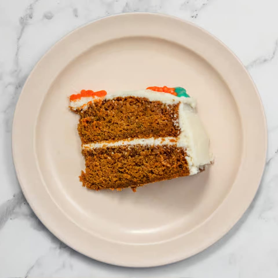 A slice of carrot cake with white frosting and orange and green carrot decorations on a plate.