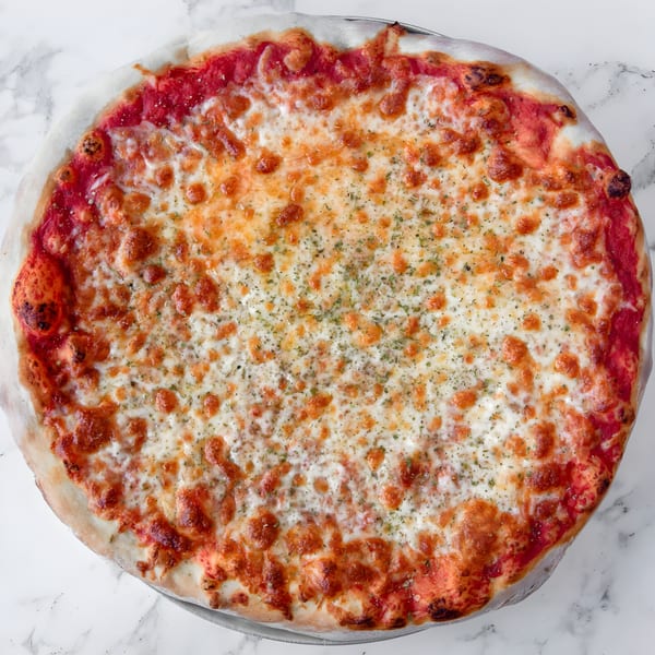 A whole Iriana's Pizza with melted cheese, red sauce, and herbs on a white marble surface.