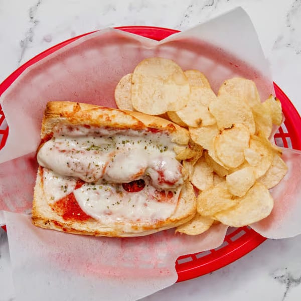 Iriana's Pizza's meatball sub with melted cheese and potato chips in a red basket.