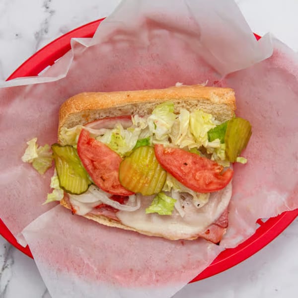 A large Iriana's Pizza sub sandwich with lettuce, tomatoes, pickles, onions, and melted cheese.