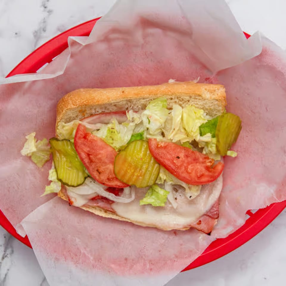 A large Iriana's Pizza sub sandwich with lettuce, tomatoes, pickles, onions, and melted cheese.
