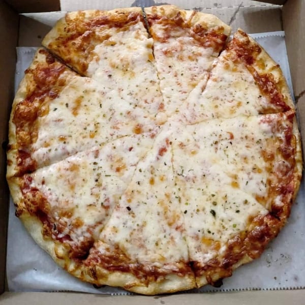 A whole Iriana's Pizza, cut into slices, with melted cheese and herbs in a cardboard box.