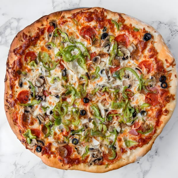 Iriana's Pizza with pepperoni, green peppers, mushrooms, onions, and black olives on a marble surface.